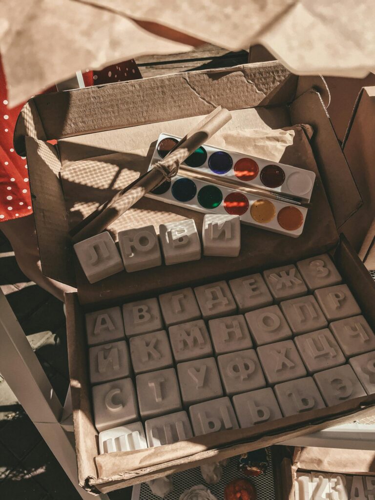 Box of Cyrillic alphabet blocks paired with vibrant watercolors and a brush.